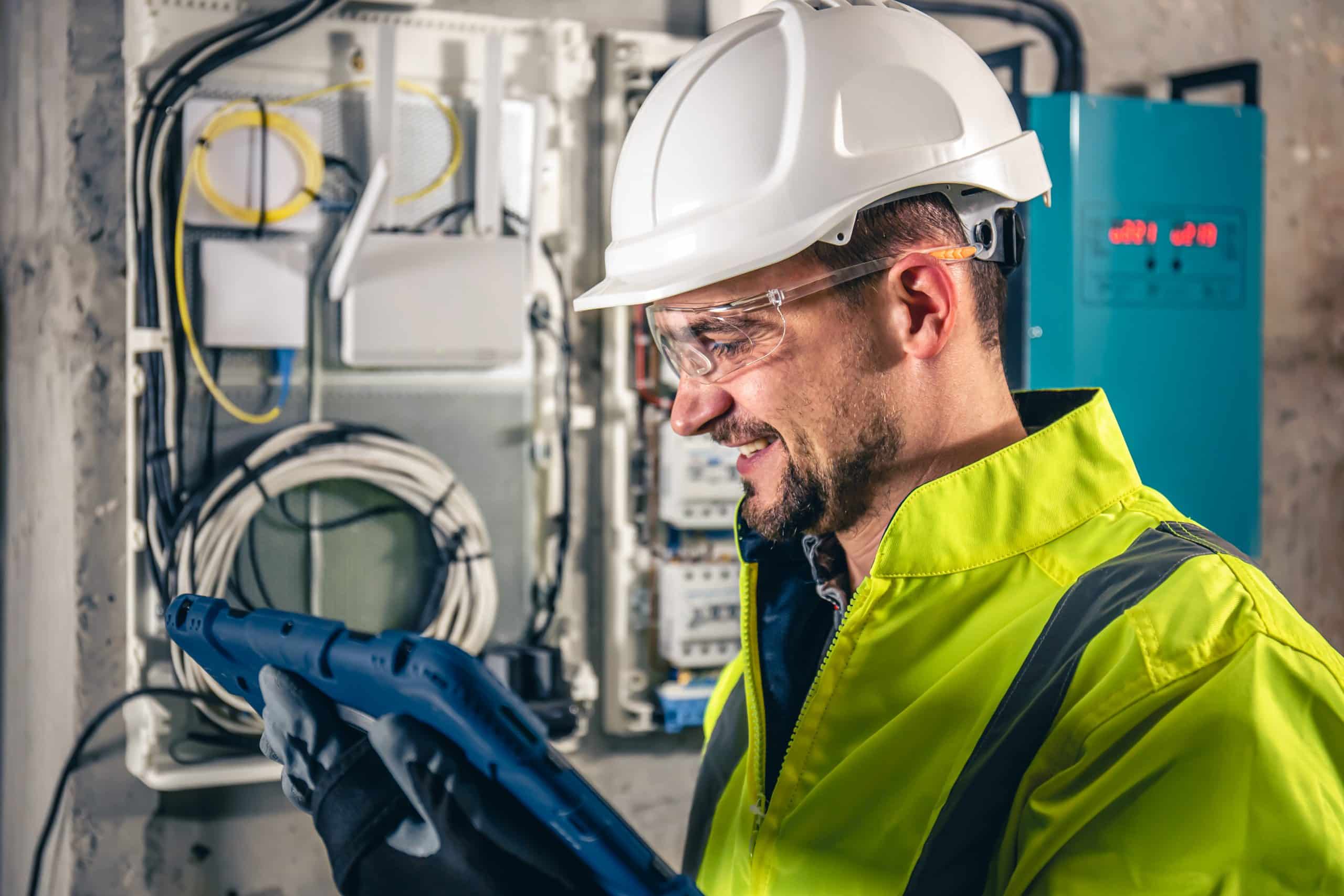 Man, an electrical technician working in a switchboard with fuses, uses a tablet.